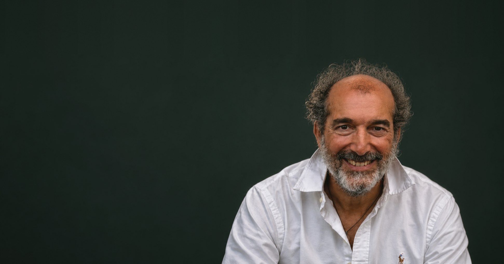 Pablo Navarro sonriendo a cámara, con camisa blanca, sobre fondo oscuro